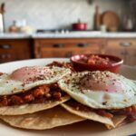 A plated Huevos Rancheros with garnishes and sides.